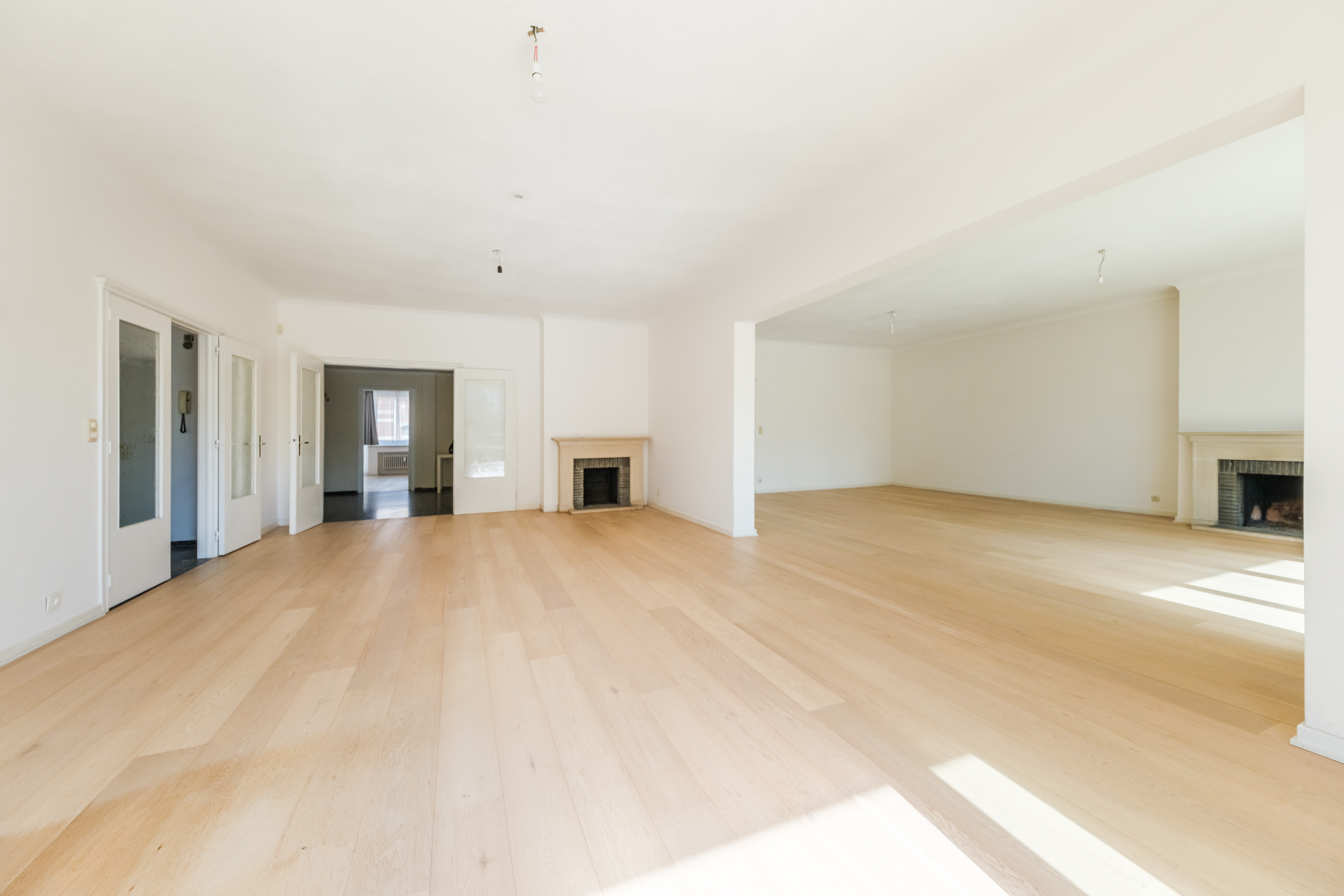 Spacious, empty living area with light wood floors, white walls, two fireplaces, and multiple doorways leading to other rooms. [AI-generated text]