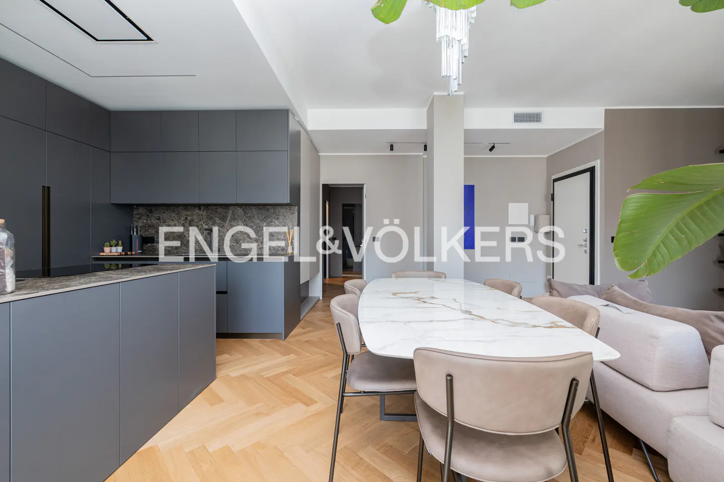 A modern open-concept kitchen and dining area with gray cabinets, a marble table, and herringbone wood floors.