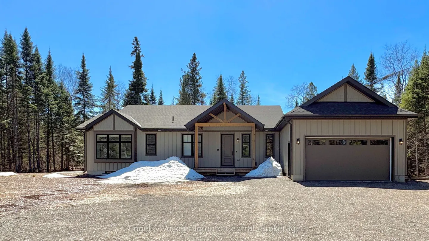Front view of a one-story beige house with a gray roof, black trim, and a two-car garage. Tall pine trees surround the house.