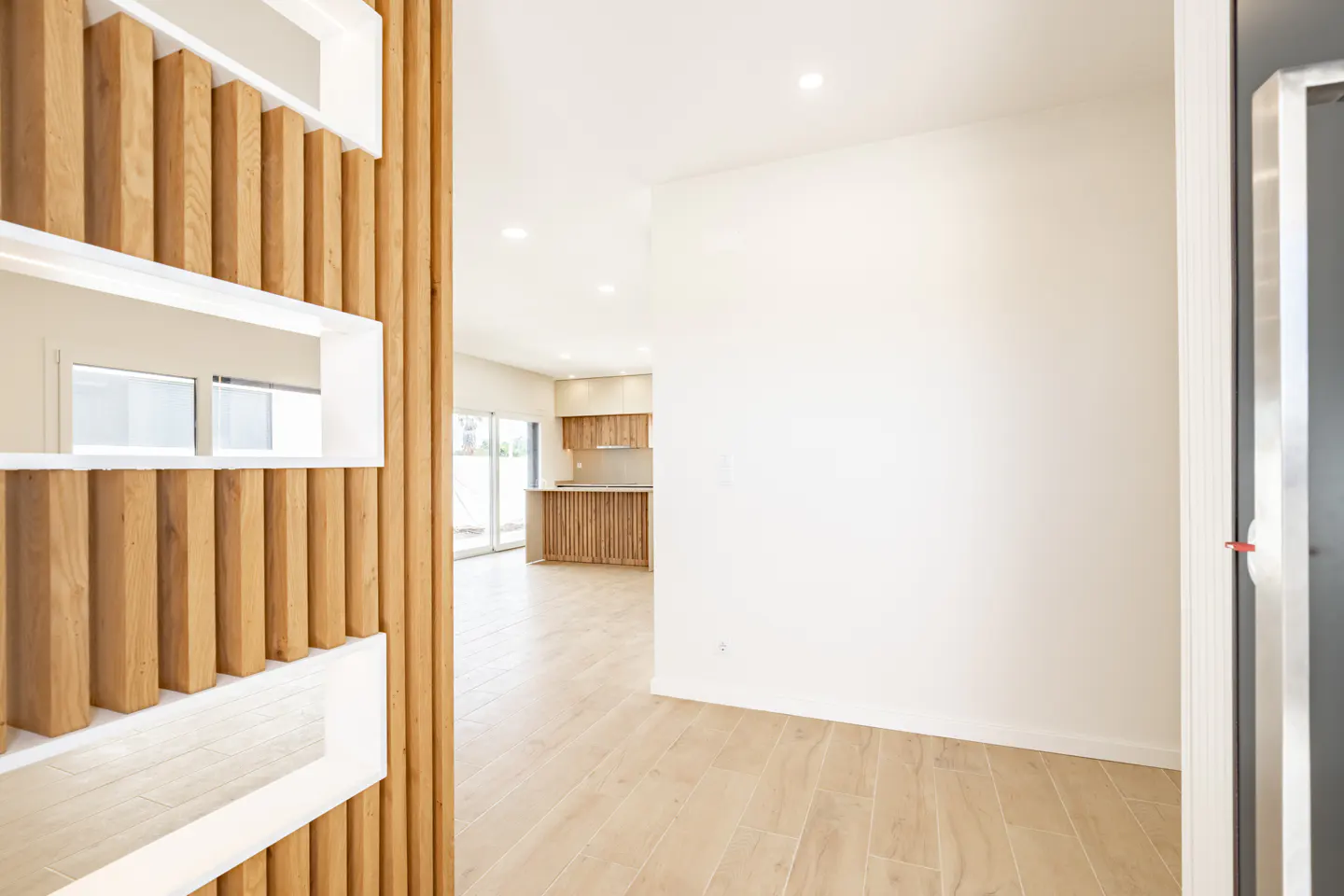 View of a bright, modern home interior featuring a decorative wooden slat room divider and a kitchen in the background.