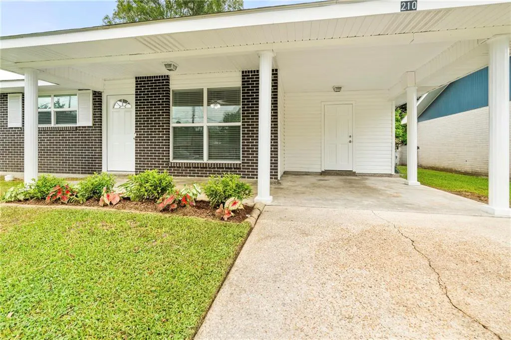 Exterior view of a single-story home with a carport, dark brick, white trim, and a green lawn.