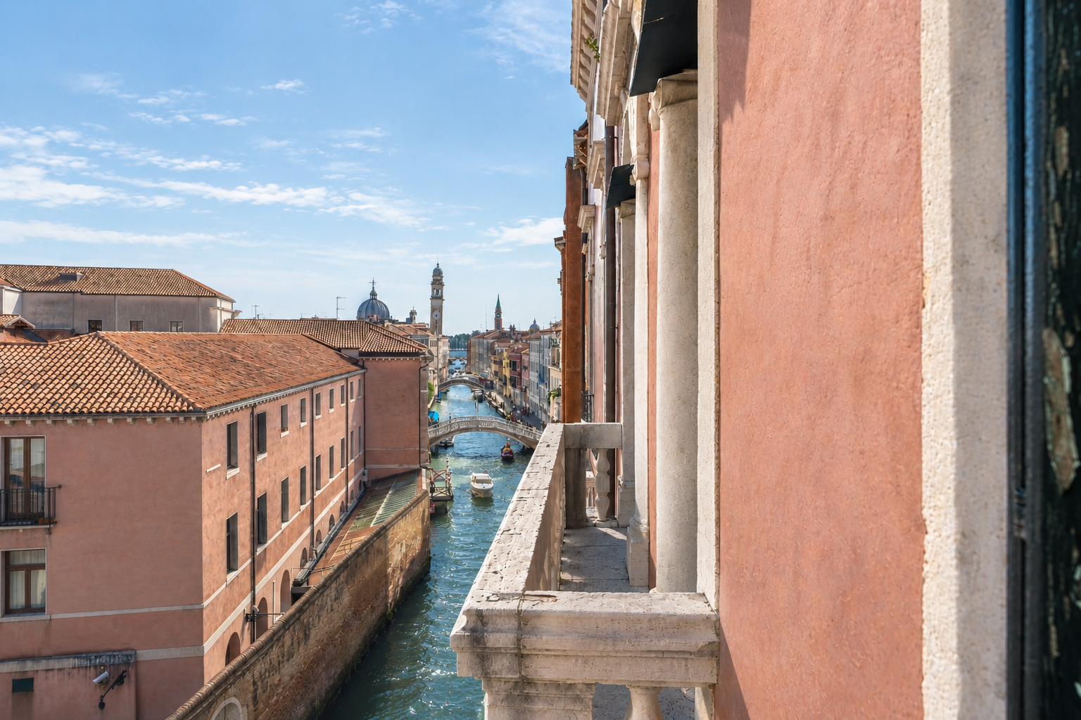 View from a balcony overlooking a narrow Venice canal with historic pink buildings, arched bridges, and boats under blue sky. [AI-generated text]
