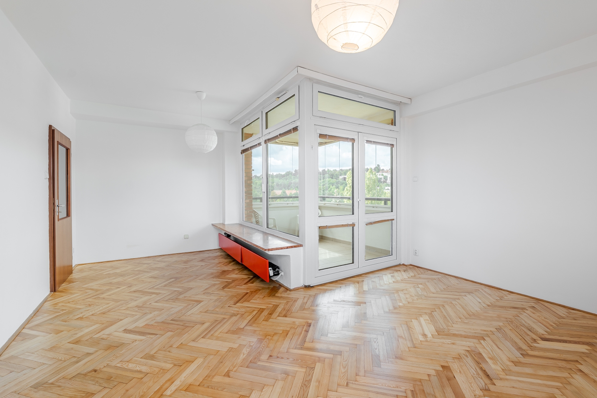 Bright room with herringbone wood floors, white walls, a red storage bench, and a glass-enclosed balcony door. [AI-generated text]