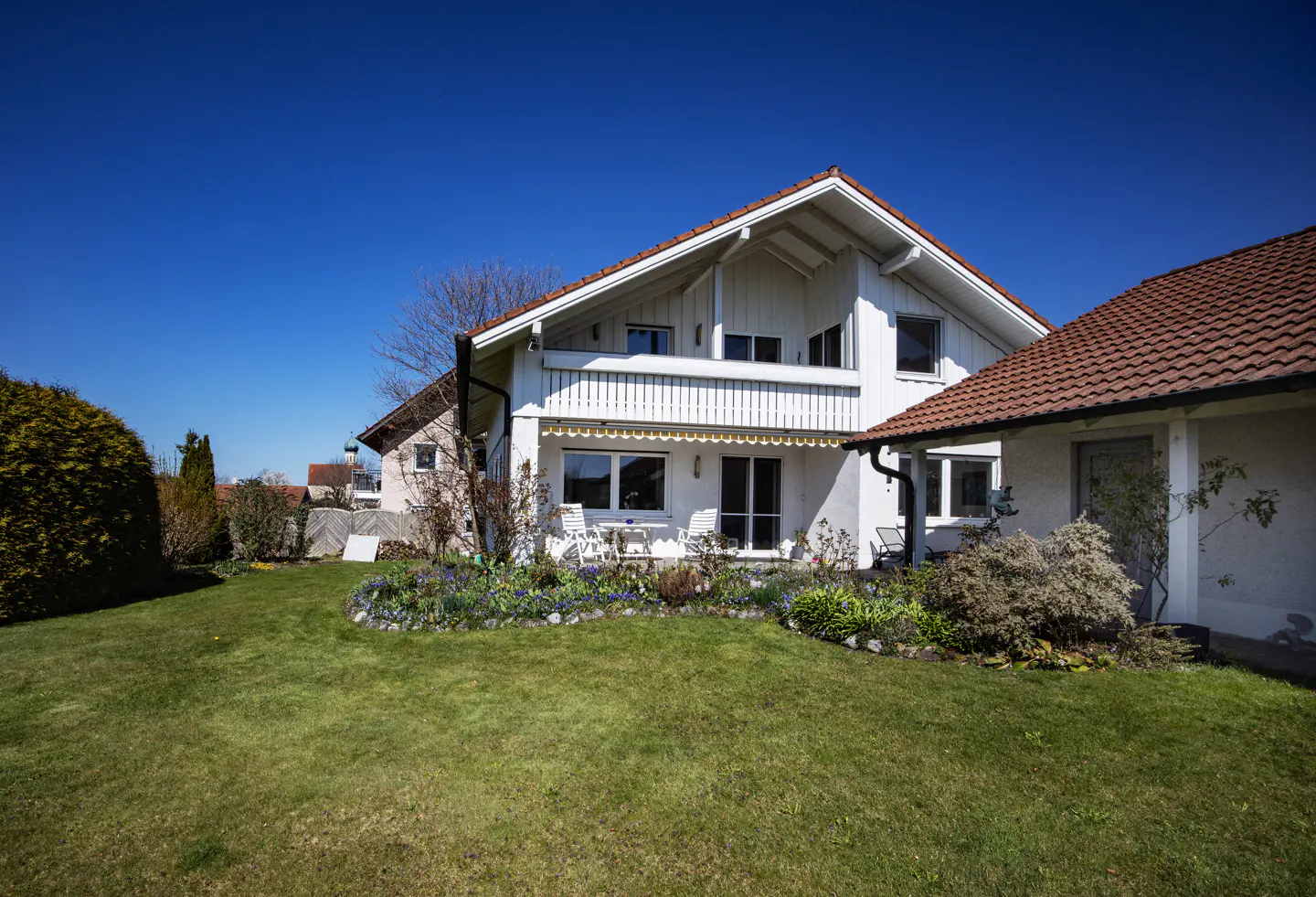 A white two-story house with a red tile roof and green lawn under a clear blue sky.