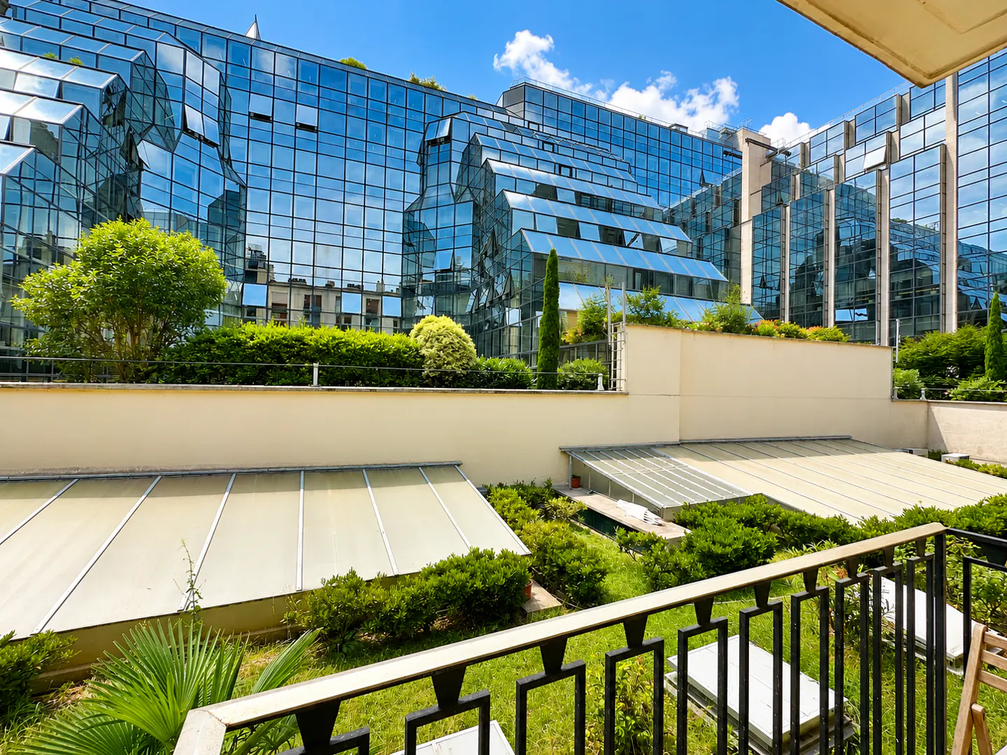 View from a balcony overlooking a modern glass office building with tiered levels, green landscaping, and skylights.
