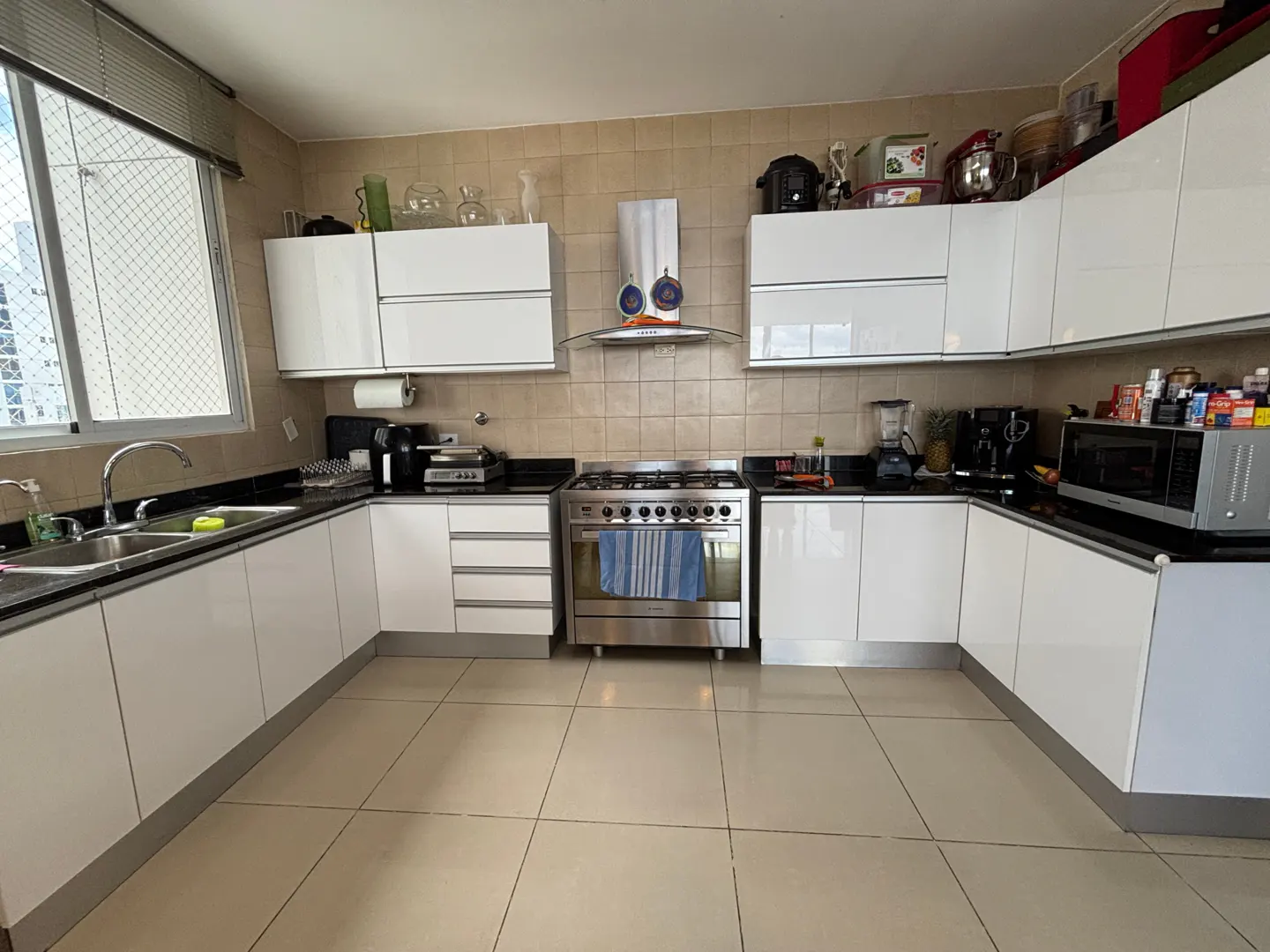 A bright kitchen with white cabinets, black countertops, and stainless steel appliances. A window is on the left side of the image.