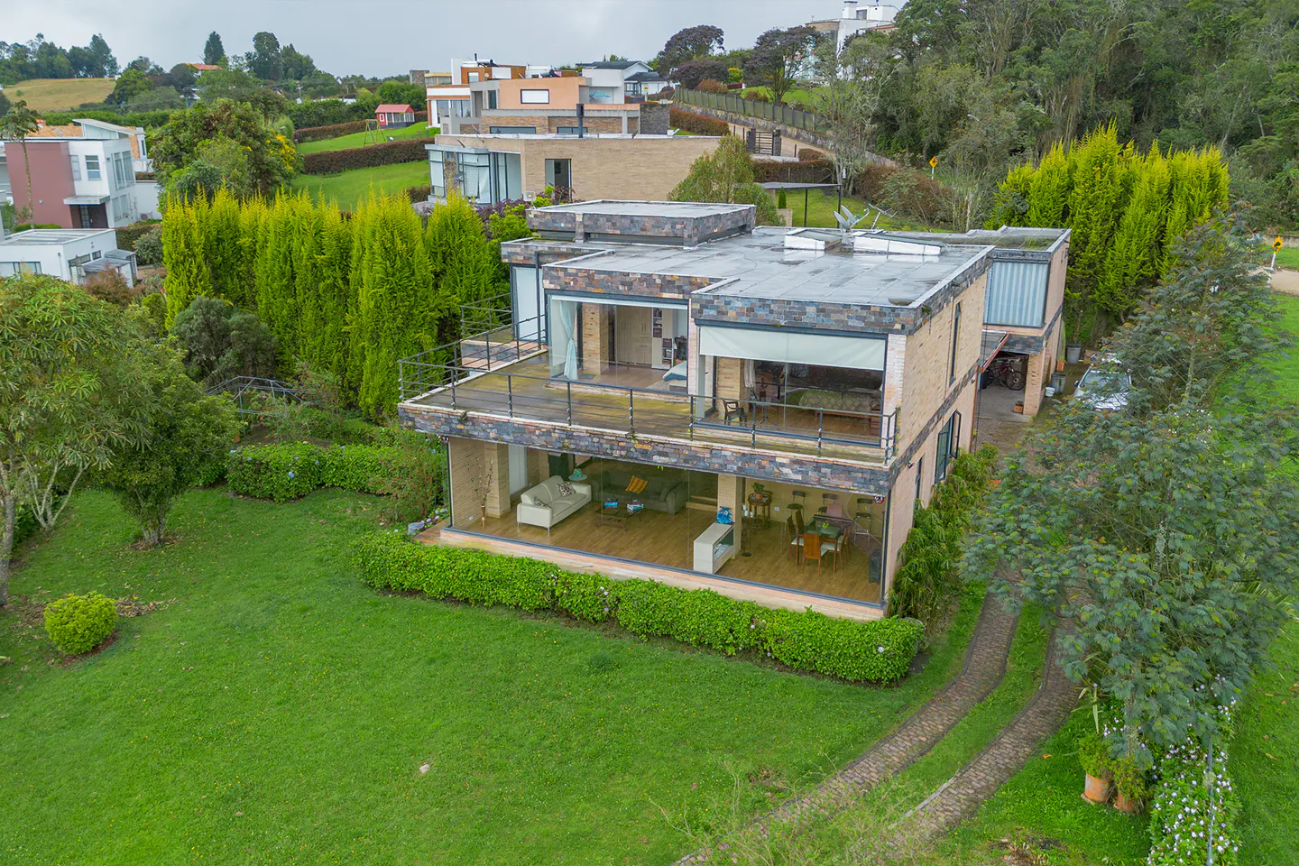 Two-story modern house with stone and glass exterior, surrounded by green lawn and trees.