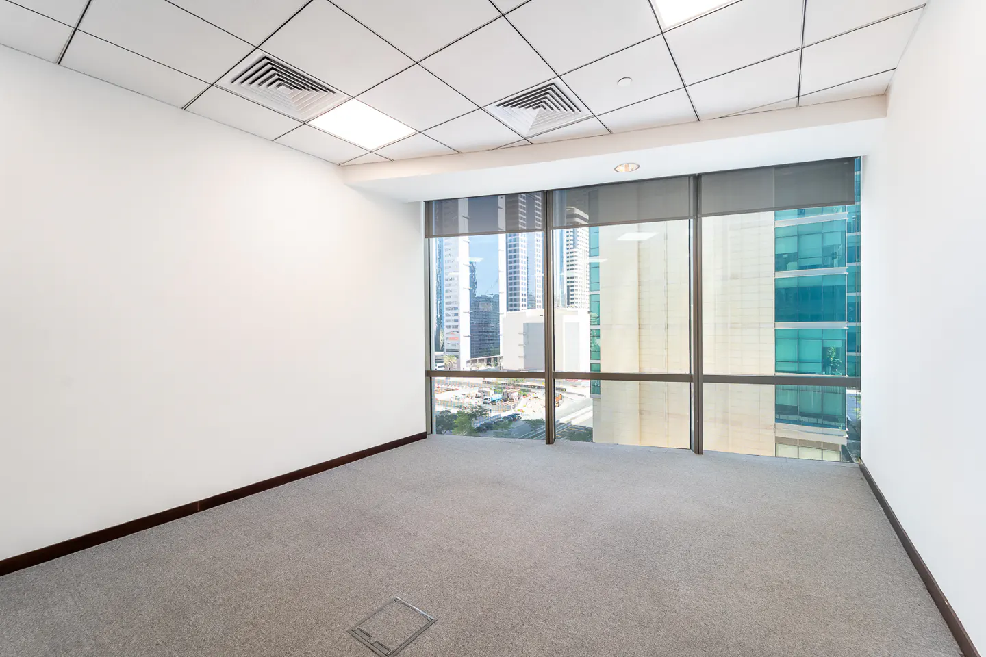 Empty office space with gray carpet, white walls, and a large window showing a city skyline.