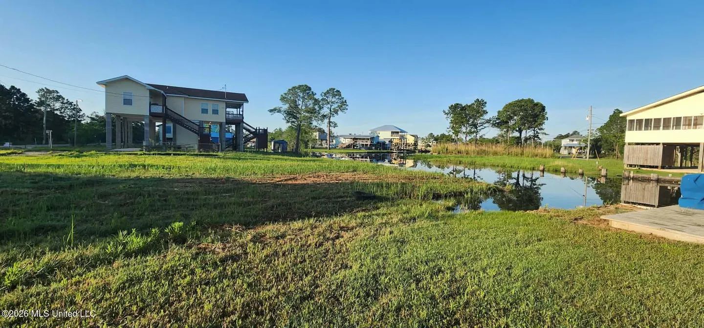 Waterfront property with a canal, green grass, and stilt houses under a clear blue sky.