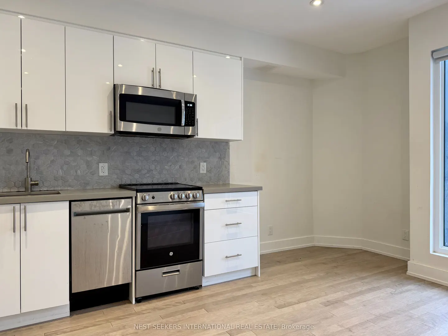 A modern kitchen with white cabinets, stainless steel appliances, gray backsplash, and light wood floors.