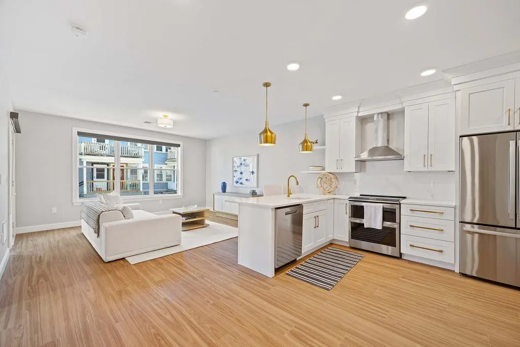 Open-concept living space with wood floors, white sofa, and kitchen with stainless steel appliances.