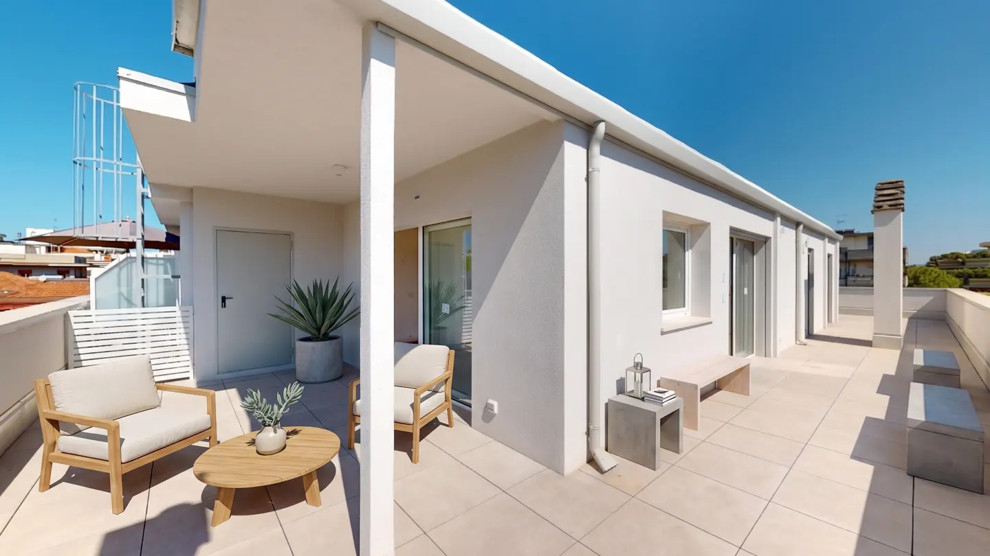 Bright rooftop patio with white walls, beige tile, and blue sky. Two chairs and a table sit near a potted plant. A bench and side table are on the right.