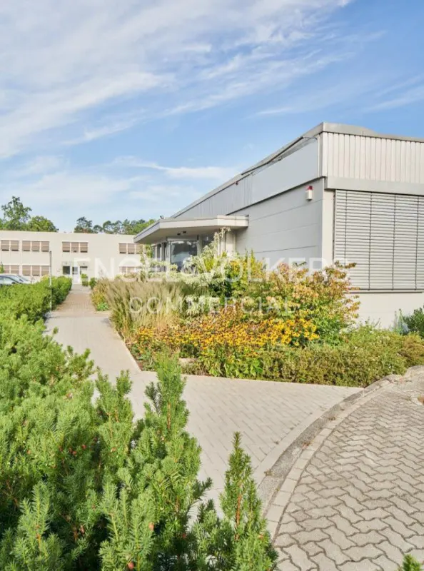 Exterior view of a modern, gray commercial building with a paved walkway and landscaped greenery under a blue sky.