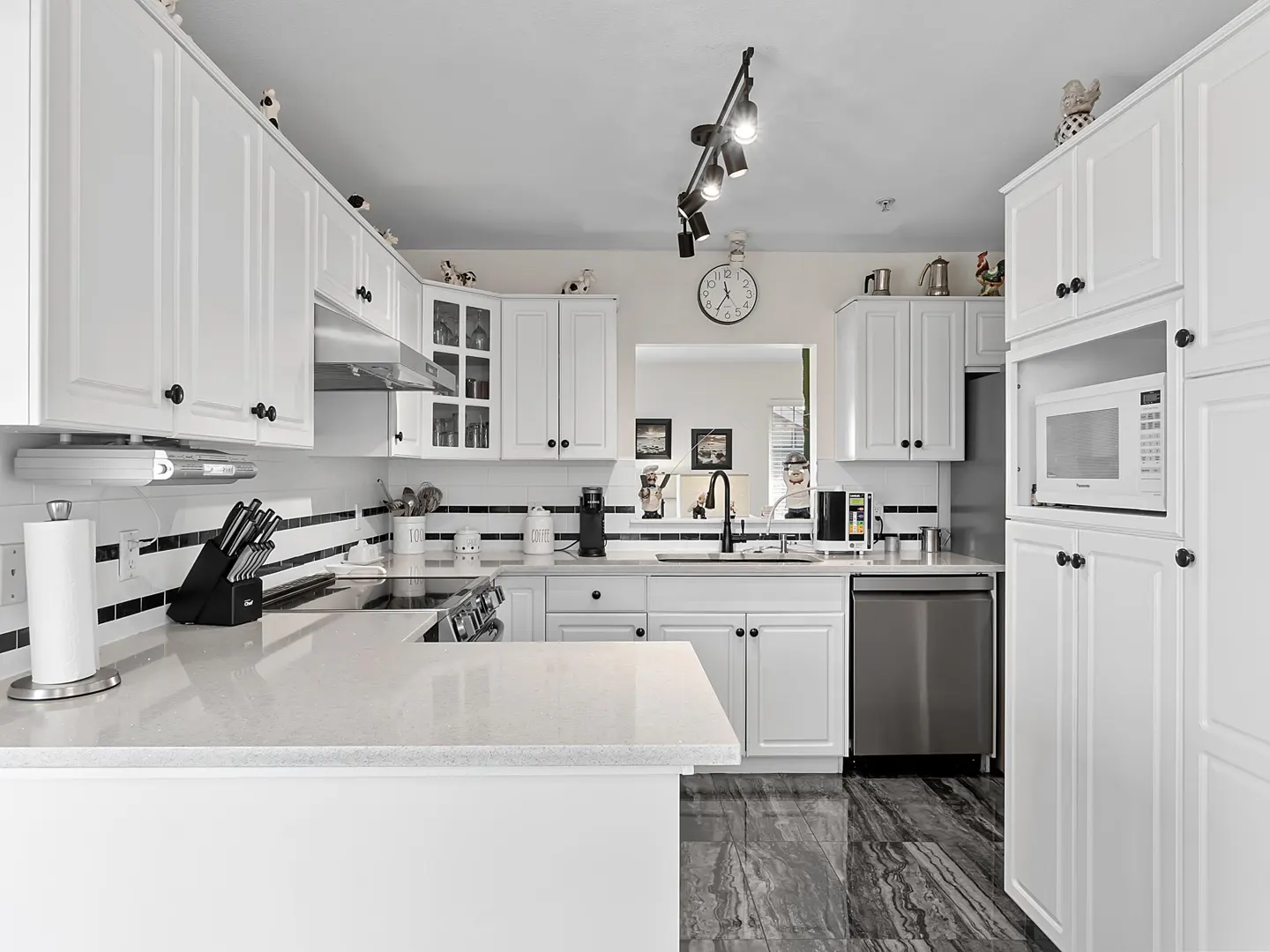 Modern kitchen with white cabinets, quartz countertops, stainless steel appliances, and dark marble-patterned tile flooring.