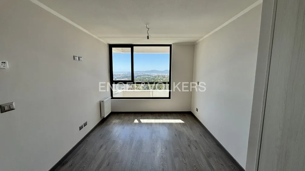 Empty room with gray wood floors, white walls, and a large window with a view of trees and mountains.