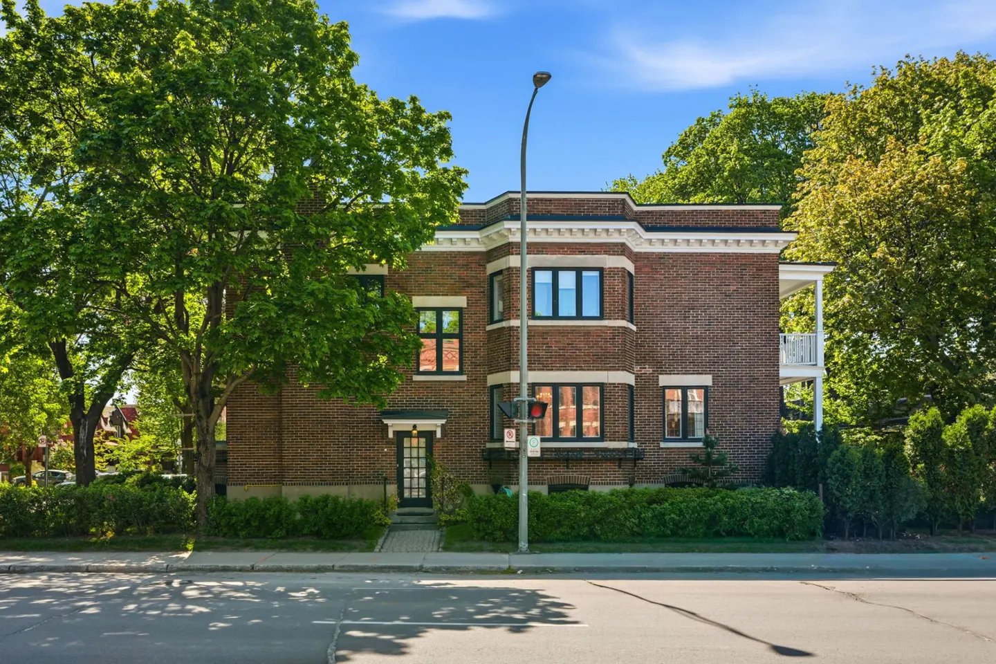 Two-story brick building with black-framed windows and a black door, surrounded by green trees and bushes.