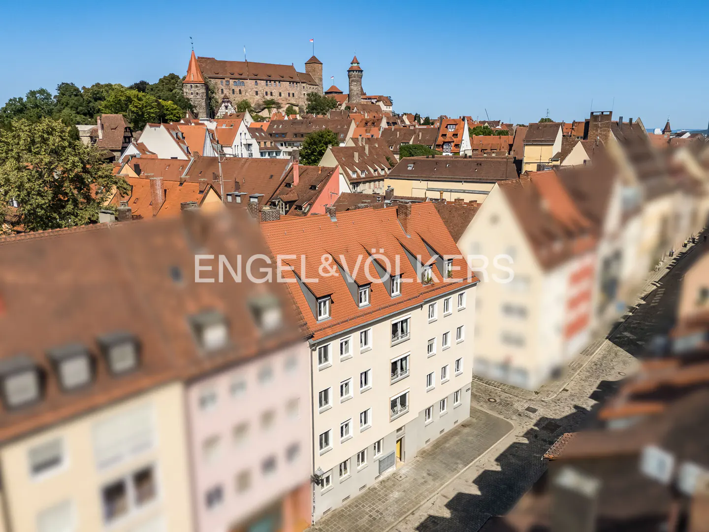 View of Nuremberg, Germany, with red-roofed buildings and a castle in the background under a blue sky. Engel & Völkers logo is visible.
