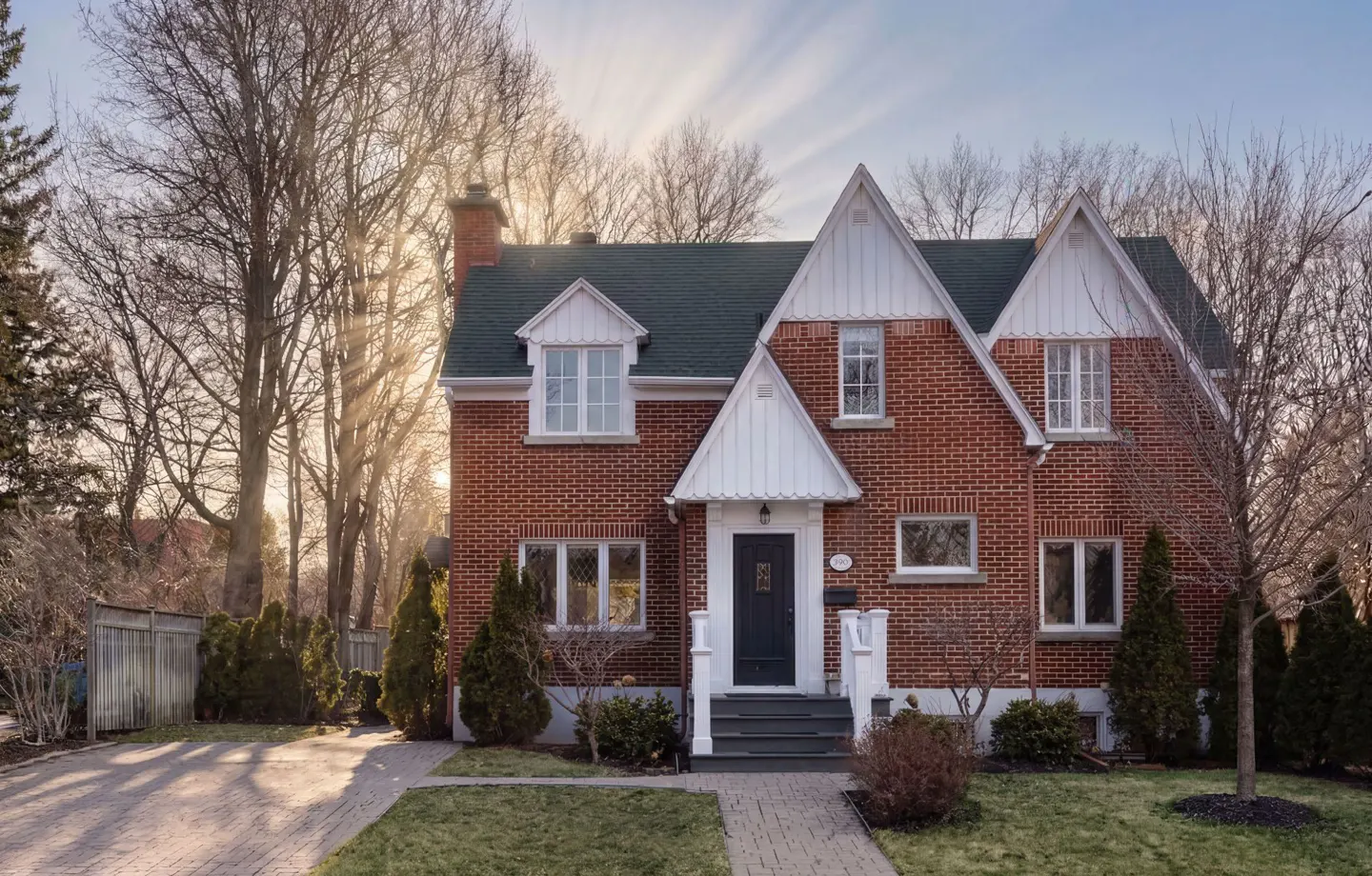 Red brick house with a dark green roof, white trim, and a dark blue front door. A brick walkway leads to the entrance. Trees surround the property.