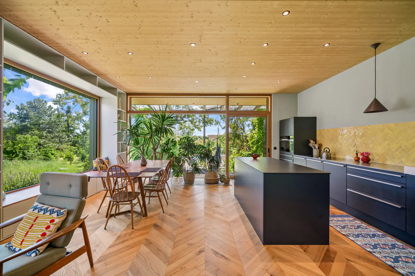 Open-concept kitchen and dining area with wood floors, large windows, and black cabinets. A table and chairs sit near the window.