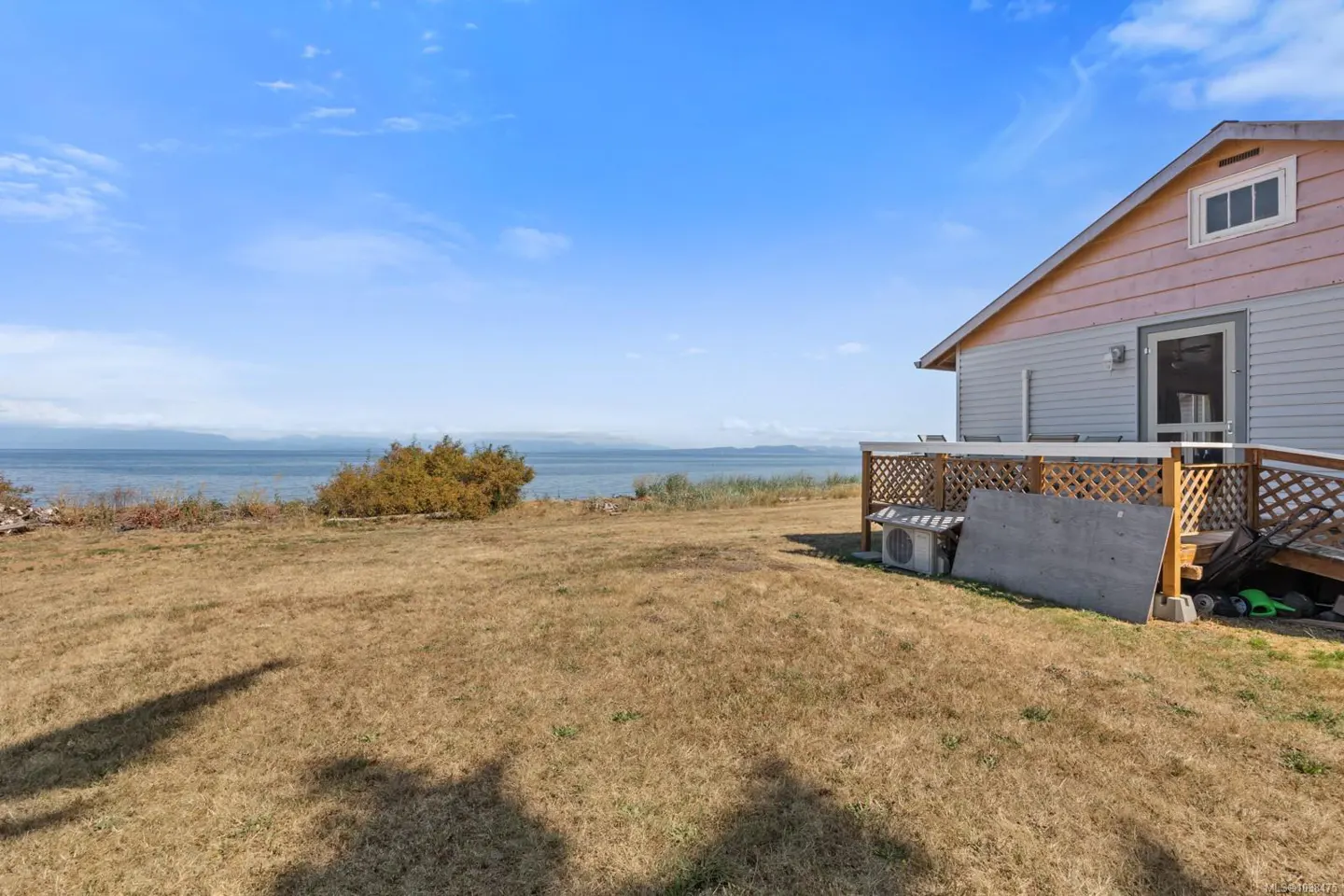 A view of a house with a deck and a large lawn, with the ocean in the background.