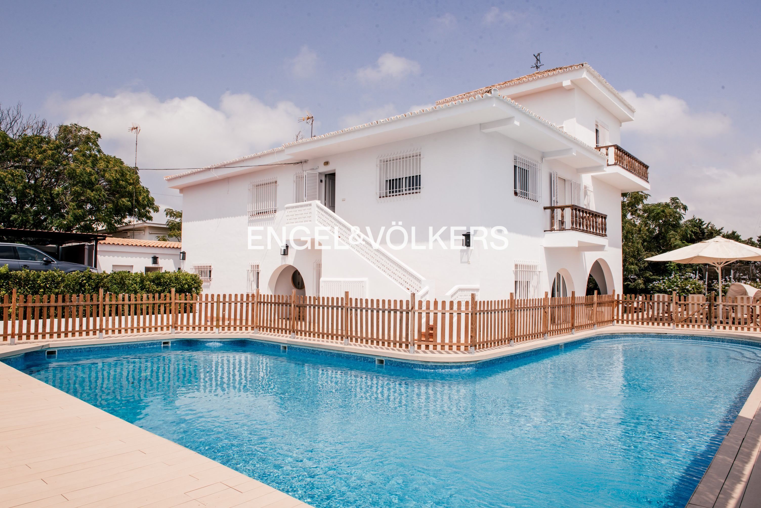 A white two-story house with a blue swimming pool and a wooden fence. [AI-generated text]