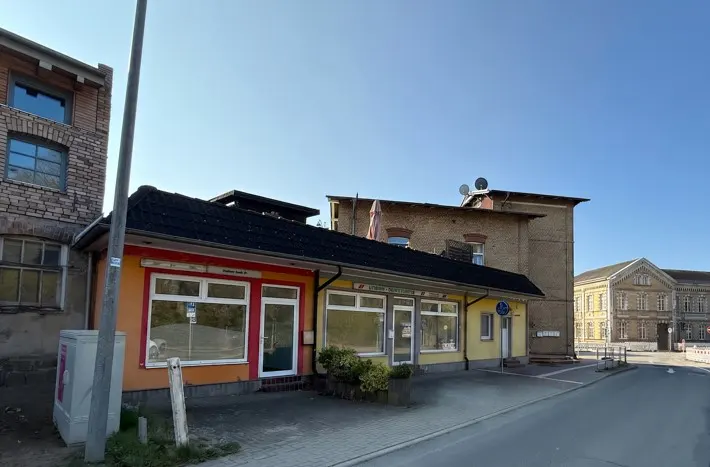 Street view of a row of small, colorful commercial buildings with large windows under a clear blue sky.