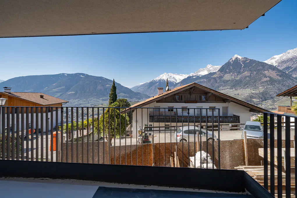 View from a balcony shows houses and cars with mountains in the background on a clear day.