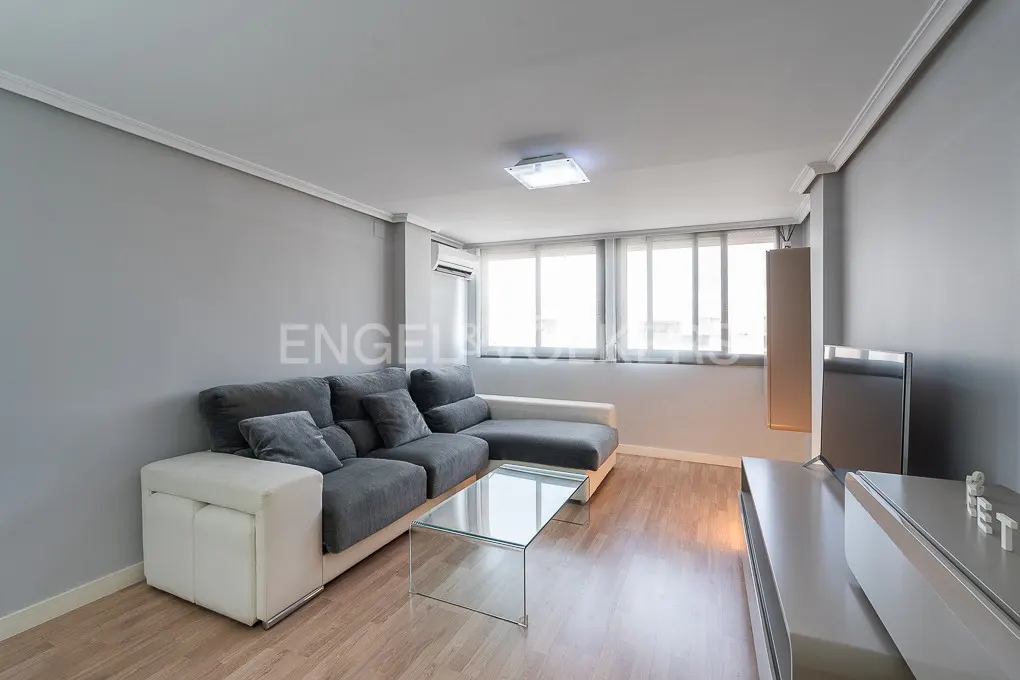Living room with gray walls, wood floors, and a gray sectional sofa with white accents. A glass coffee table sits in front of the sofa. A TV and console are on the right.