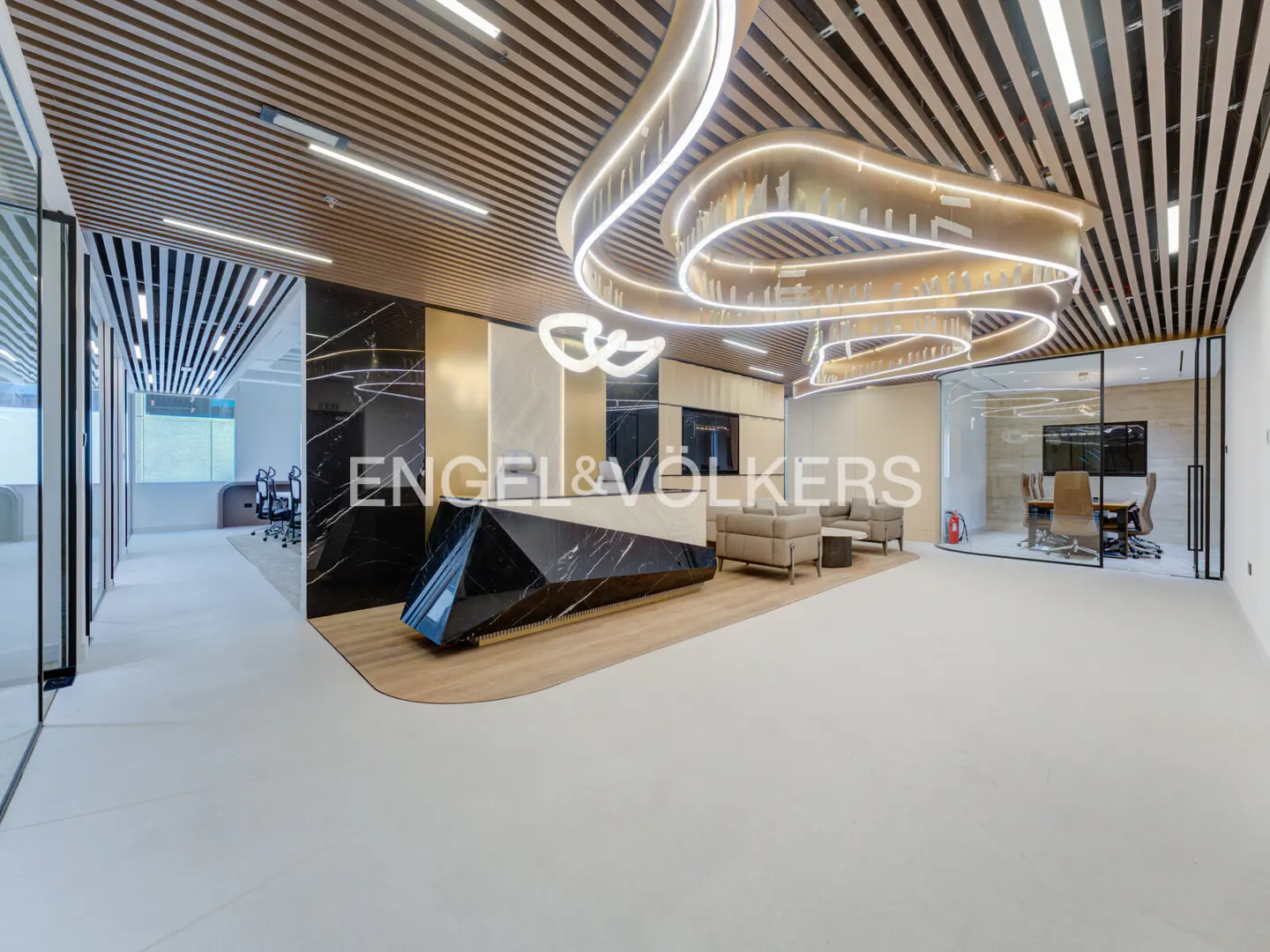 Engel & Völkers office lobby with a black marble reception desk, beige sofas, and a glass-walled conference room. The ceiling has wood slats and modern lighting.