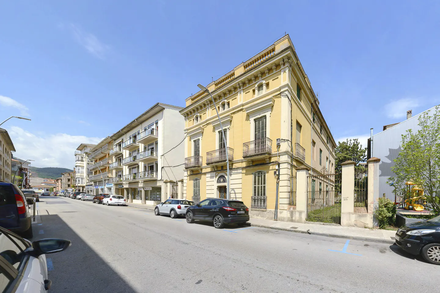 A yellow historic building on a sunny street with parked cars and a clear blue sky.