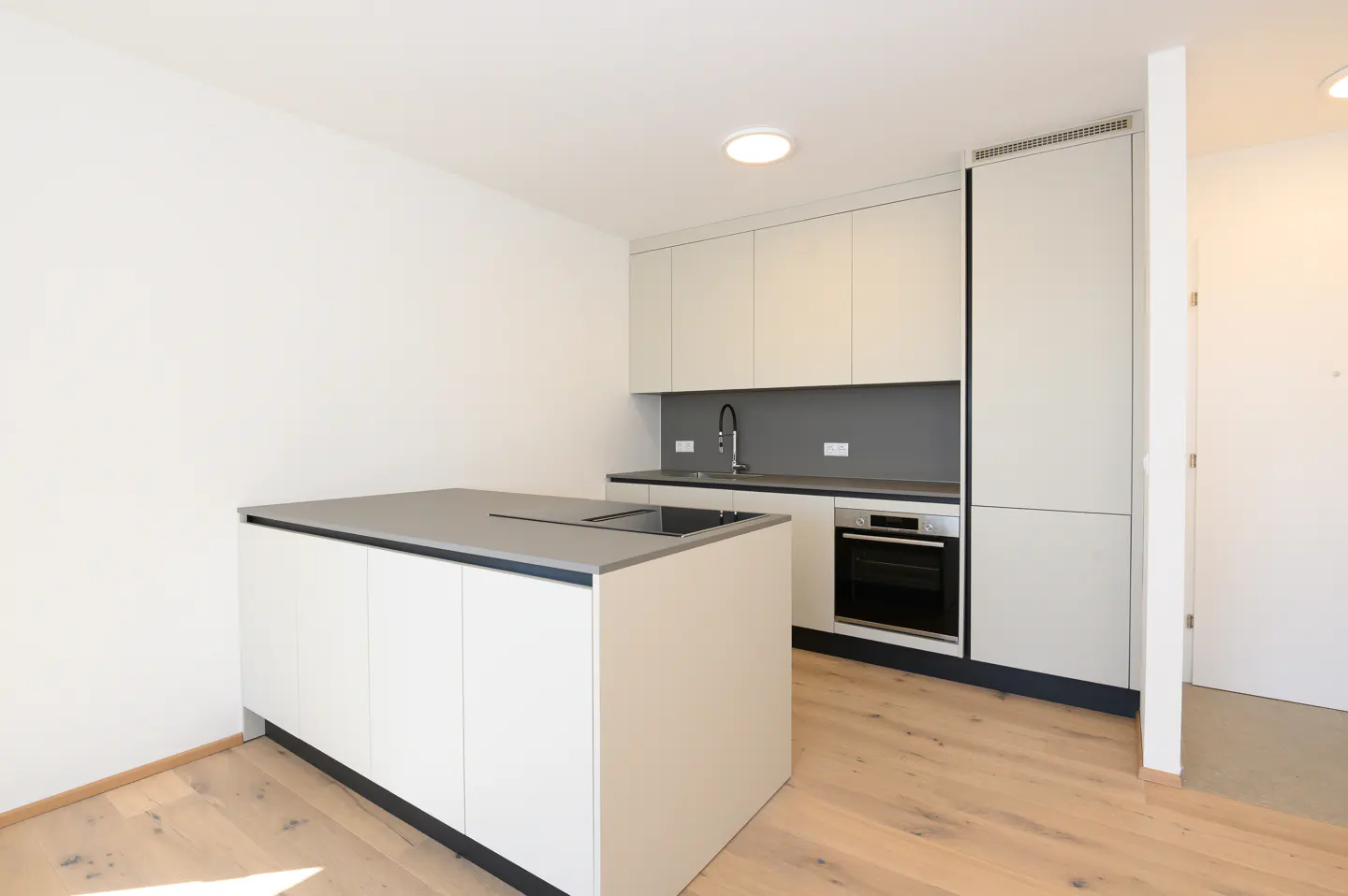 Modern kitchen with white cabinets, gray countertops, and wood floors. A kitchen island stands in the center.
