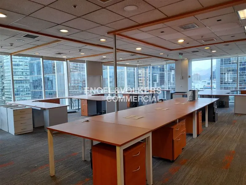 Bright, empty office space with desks, orange cabinets, and large windows with city views.