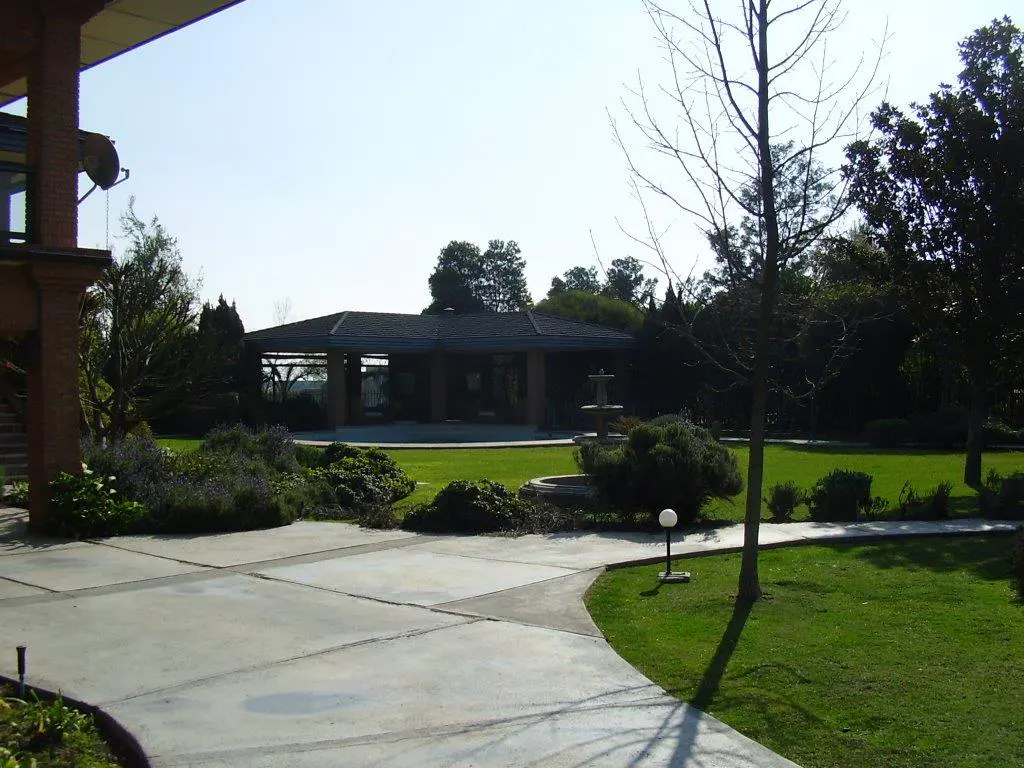 A backyard with a covered patio, fountain, green grass, and a concrete walkway.