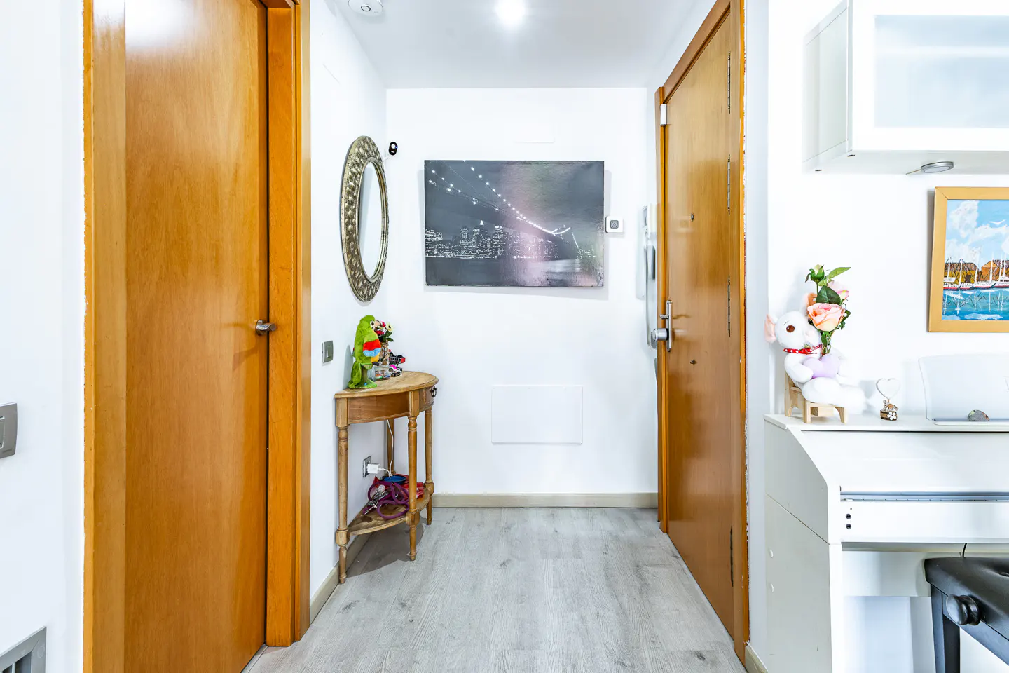 Hallway with light gray floors, white walls, and two wooden doors. A table with a mirror and decor sits near a black and white bridge photo.