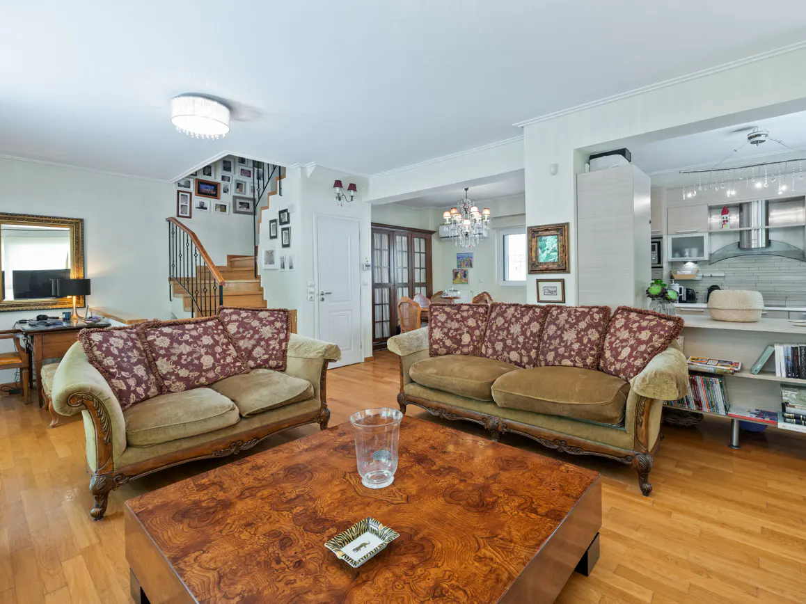 Spacious living room with two brown sofas, a large wooden coffee table, hardwood floors, and an open-plan kitchen.
