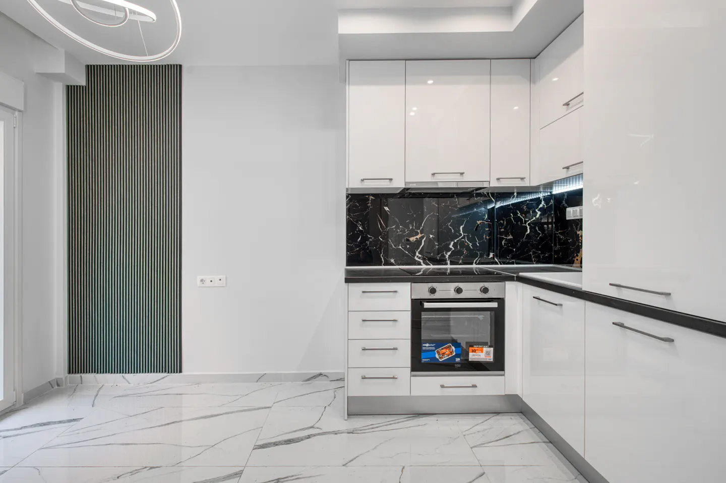 A modern kitchen with white cabinets, black marble backsplash, and marble tile flooring.