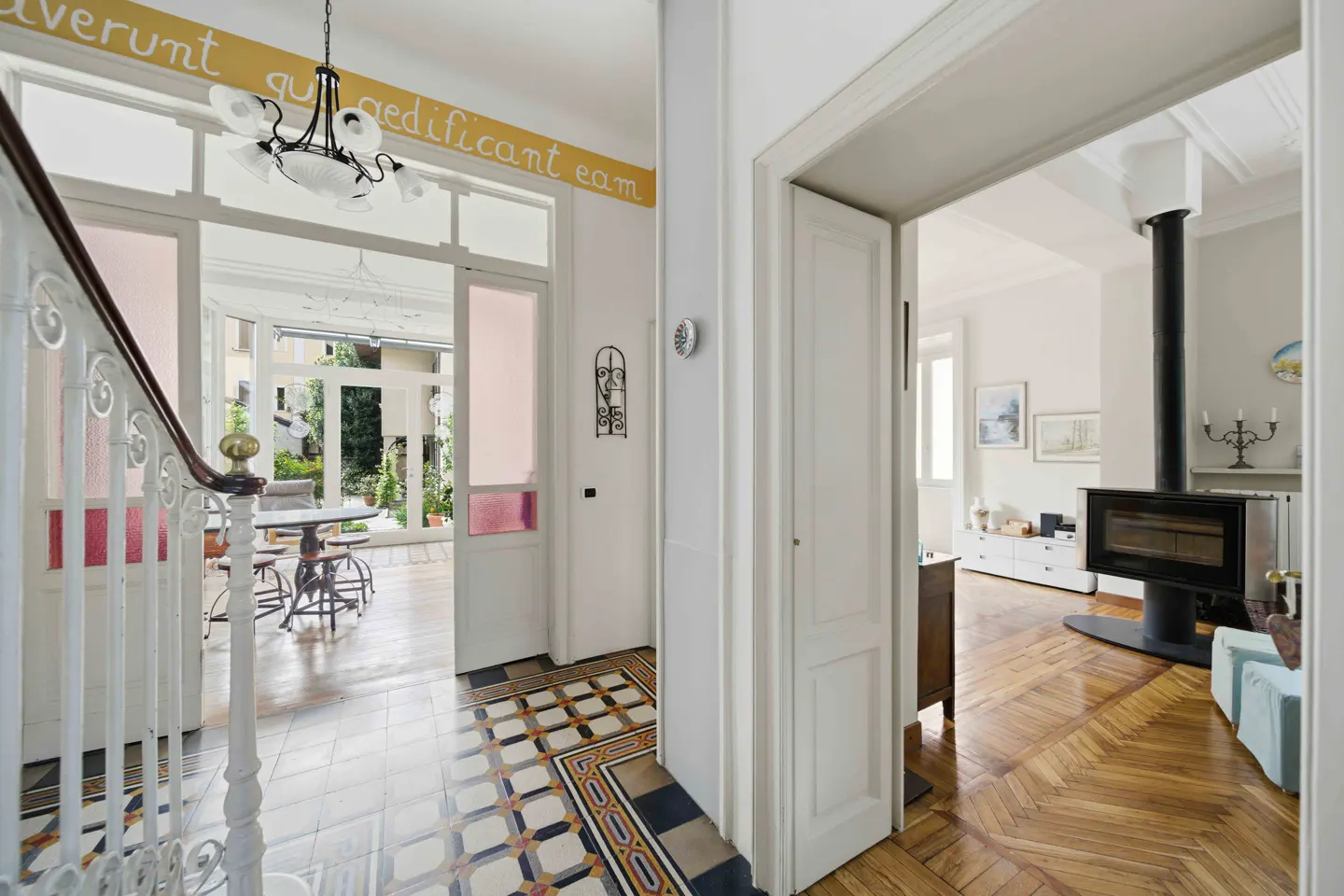 Hallway view into a bright living room with a fireplace. Tiled floor transitions to wood. White walls and doors.