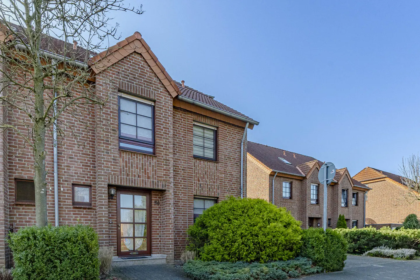 Row of brick townhouses with red tile roofs, green bushes, and a clear blue sky.