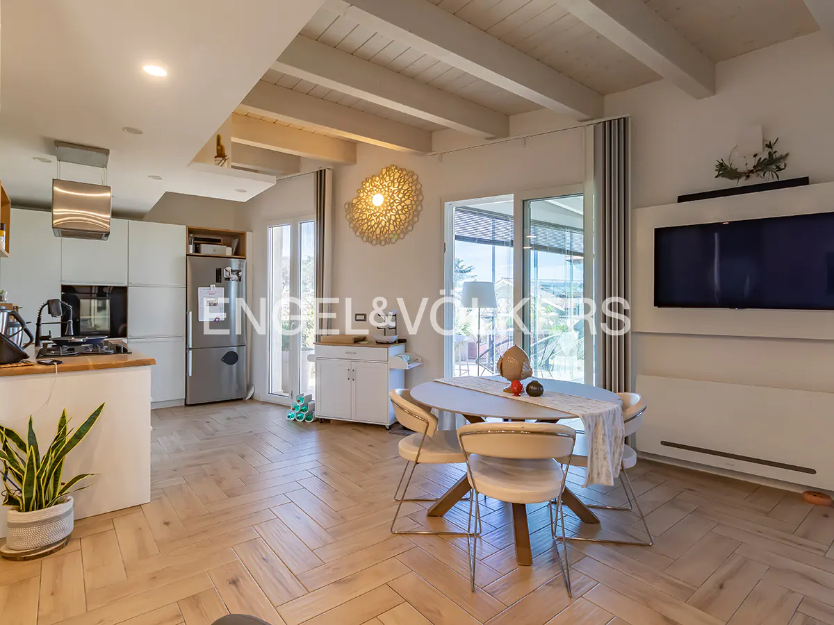 Modern open-plan kitchen and dining area with light wood herringbone floors, white cabinets, and a round dining table.