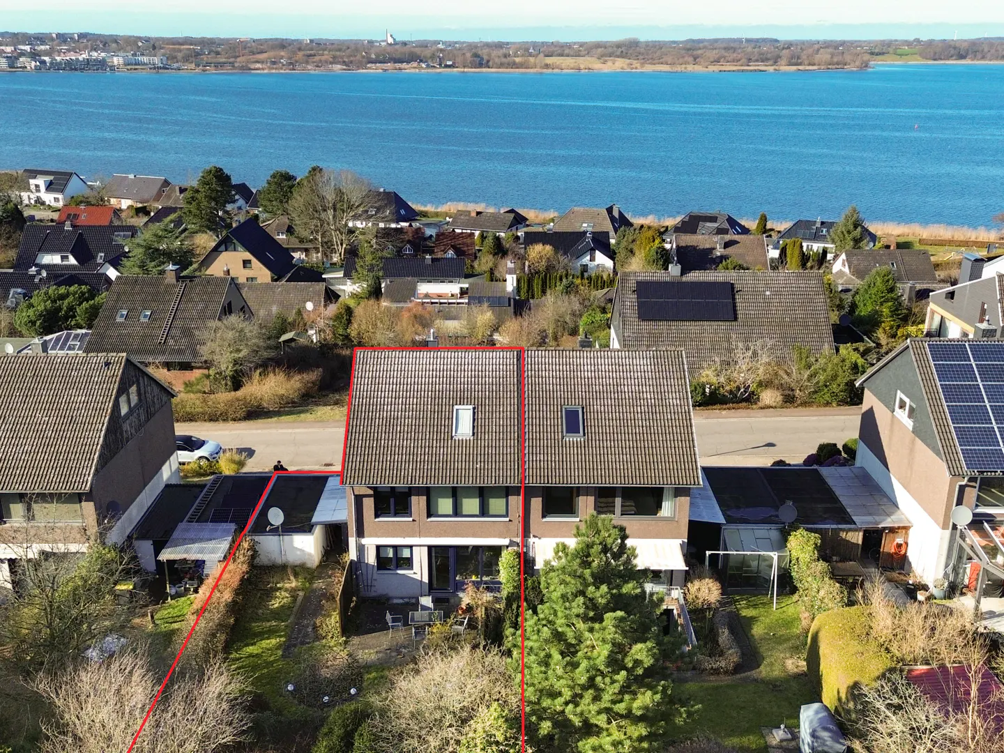 Aerial view of a semi-detached house with a red outline, featuring a backyard and a scenic waterfront view in the distance.