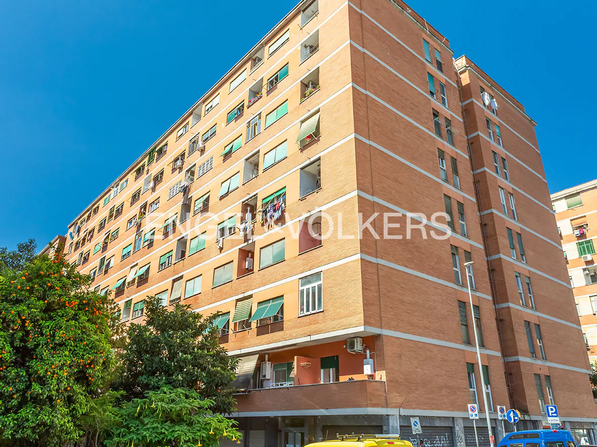 Exterior view of a tall, brick apartment building with green awnings under a clear blue sky. Trees with orange fruit are in the foreground.