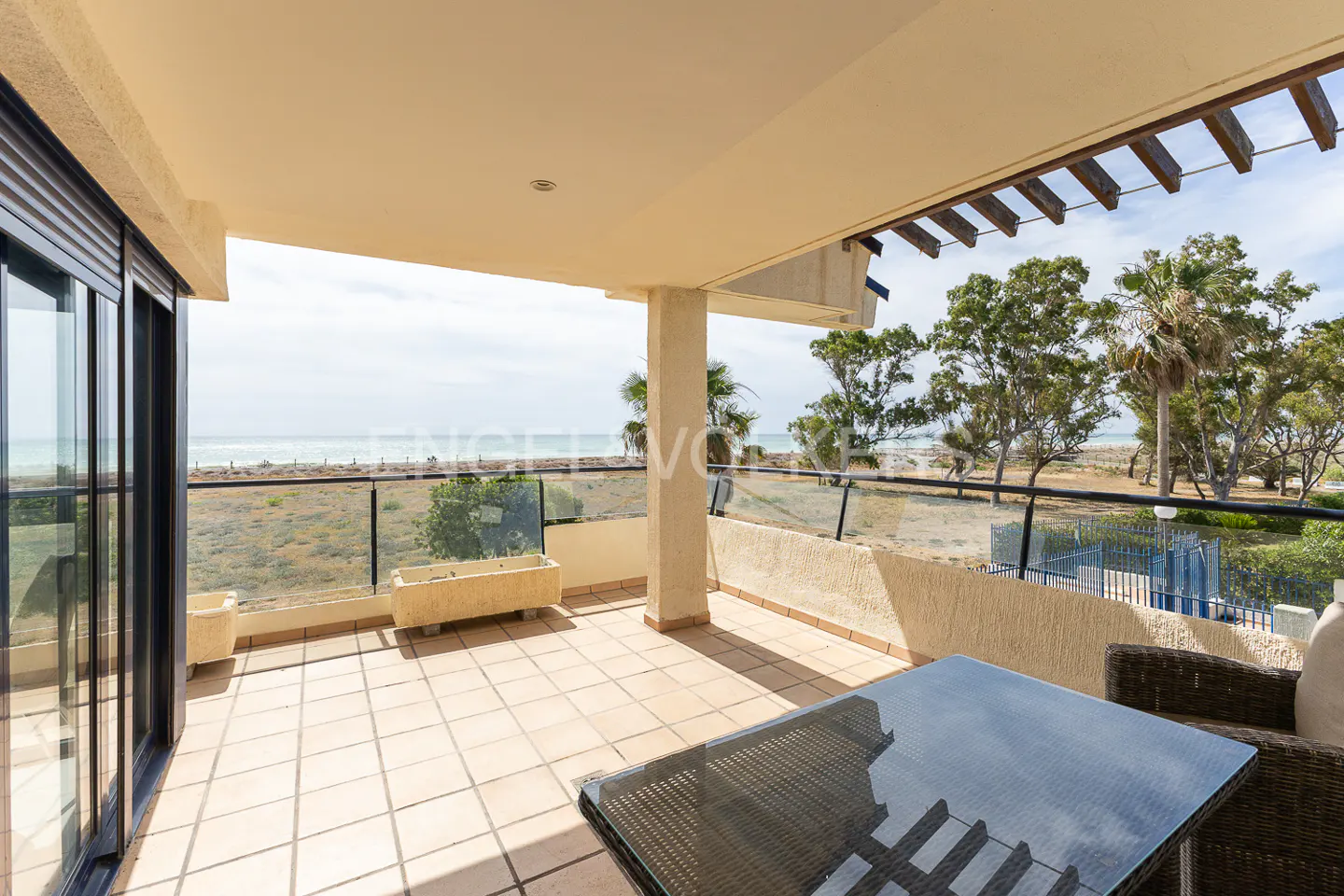 Balcony with tile floor, glass railing, and ocean view. Wicker furniture and planters add to the outdoor living space.