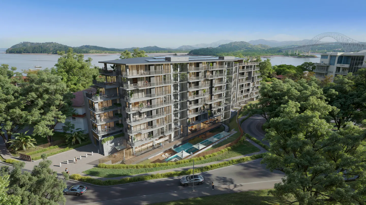 Exterior view of a modern, multi-story gray apartment building with balconies, a pool, and lush green trees, with a bridge and mountains in the background.