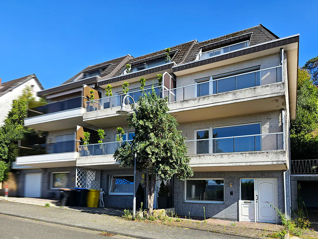 Three-story gray apartment building with balconies and large windows under a clear blue sky.