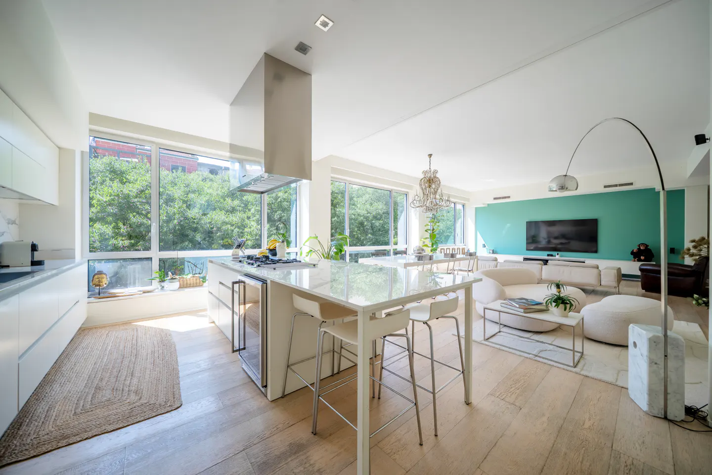 Modern open-concept kitchen and living area with white cabinets, a kitchen island, and a teal accent wall with a TV.