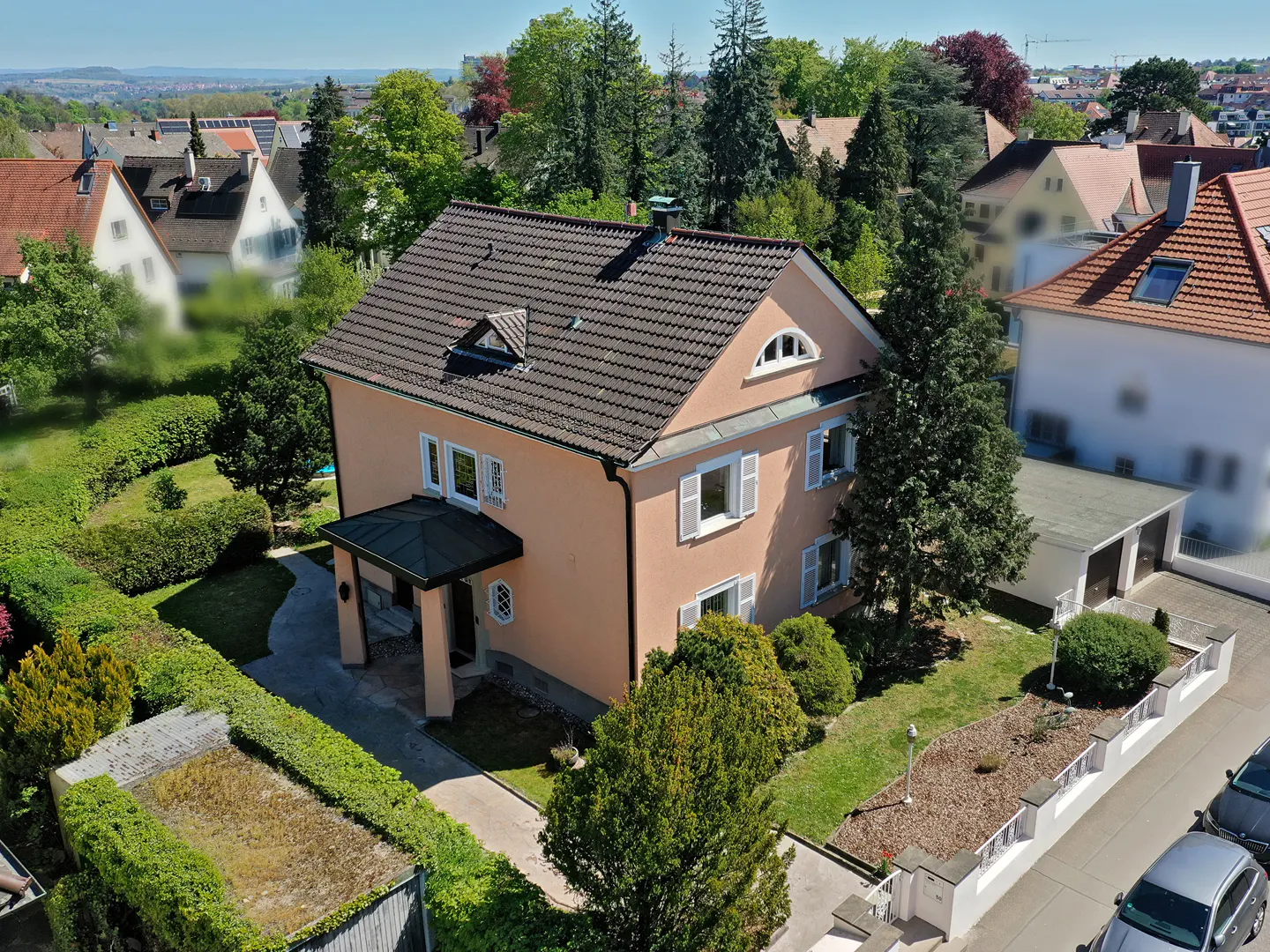 Aerial view of a two-story peach house with a brown roof, white shutters, and green landscaping.