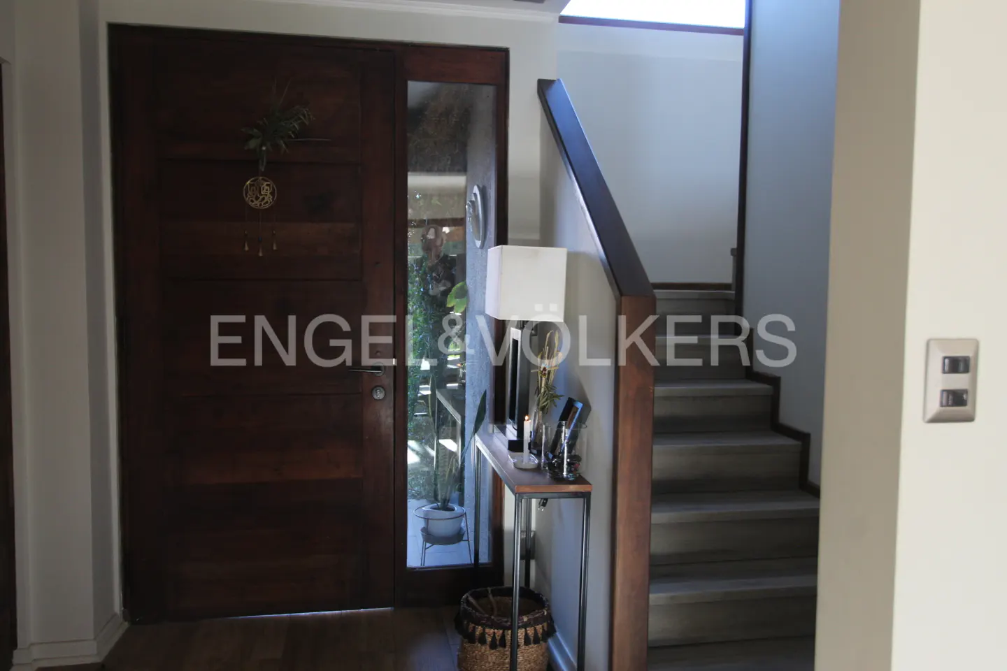 Entryway with a dark wood door, glass sidelight, console table with lamp, and concrete stairs with dark wood railing.