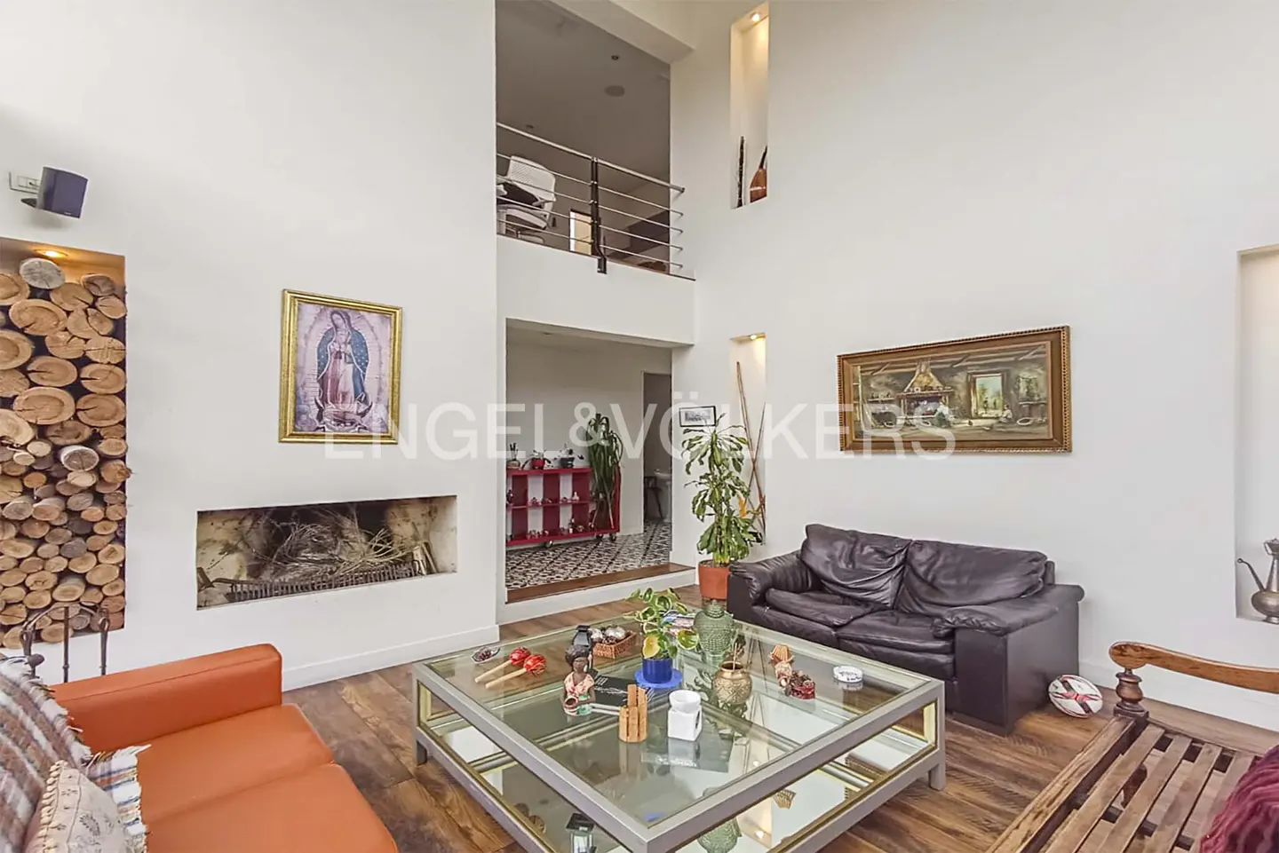 Bright living room with high ceilings, a fireplace, and a glass coffee table. Orange sofa and black leather couch. Artwork on the walls.
