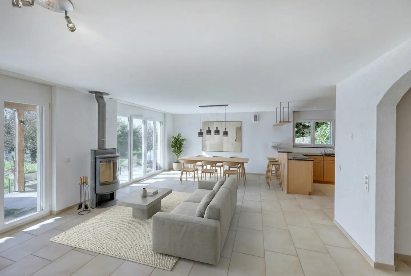 Bright, open-concept living space with a fireplace, dining table, and kitchen. Neutral tones and natural light create a modern, airy feel.