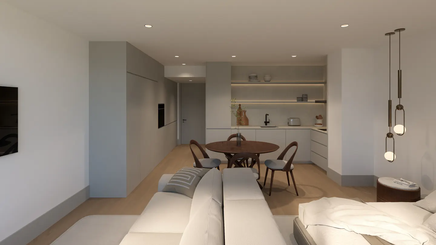A modern studio apartment with a white sofa, round wooden table, and a small kitchen area. Pendant lights hang above a bed.